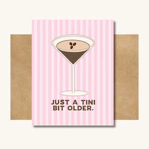 Op de afbeelding: Wenskaart met een roze en witte gestreepte achtergrond. De kaart toont een martini glas illustratie met een bruin drankje en drie koffiebonen. De tekst luidt: "JUST A TINI BIT OLDER."