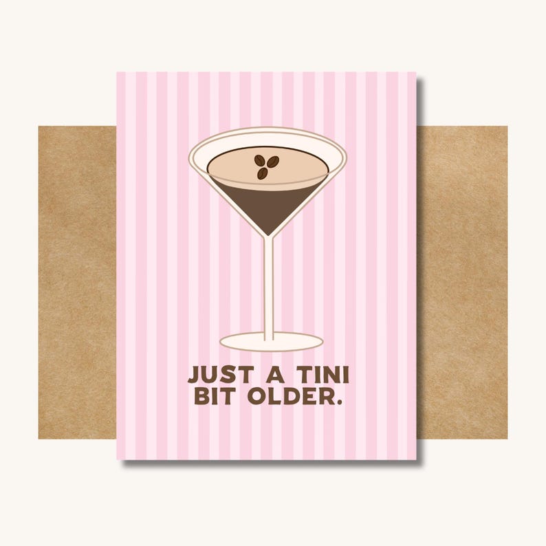 Op de afbeelding: Wenskaart met een roze en witte gestreepte achtergrond. De kaart toont een martini glas illustratie met een bruin drankje en drie koffiebonen. De tekst luidt: "JUST A TINI BIT OLDER."