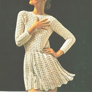 May include: A white crochet dress with long sleeves and a flared skirt. The dress features a detailed openwork pattern and a fitted waist. The model is wearing the dress against a dark background. The dress is a vintage style.