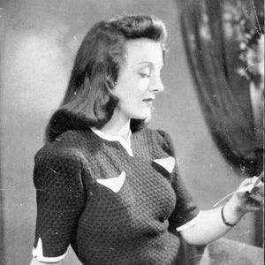 May include: Vintage black and white photograph of a woman wearing a dark textured knit sweater with white trim and accents. The image includes text at the top that reads "PATONS BEEHIVE FINGERING, 3-PLY" and the number "124".