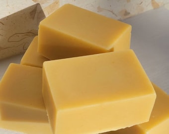 May include: Four rectangular bars of yellow soap stacked on top of each other. The soap is a light yellow color and has a smooth, matte finish.
