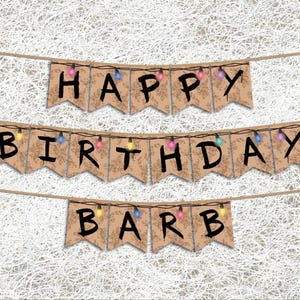 May include: A birthday banner reading "HAPPY BIRTHDAY BARB". The brown pennants with black lettering are strung with fairy lights. The background is a white, textured pattern.