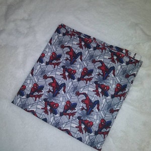 Könnte beinhalten: Grauer Stoff mit einem sich wiederholenden Muster aus roten und blauen Spiderman-Figuren auf einem Spinnennetz-Design.