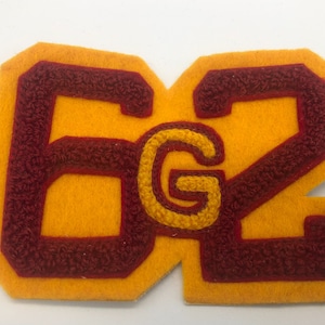 May include: A yellow felt patch with the number "62" in maroon felt with a maroon "G" in the center. The patch is likely a school or team patch.