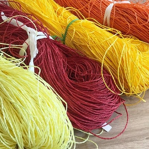 May include: Four spools of colorful string, yellow, orange, red, and light yellow. The spools are arranged in a row, with the yellow spool at the top and the light yellow spool at the bottom.