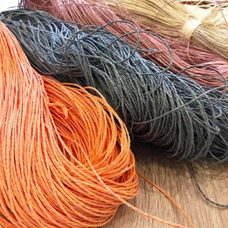 May include: Close-up of four spools of colorful string. The string is made of natural fibers and is available in orange, gray, pink, and beige.