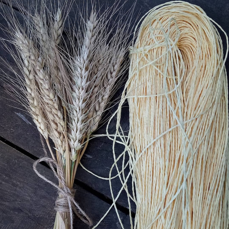 May include: A bundle of dried wheat stalks tied together with twine, next to a spool of natural beige twine.