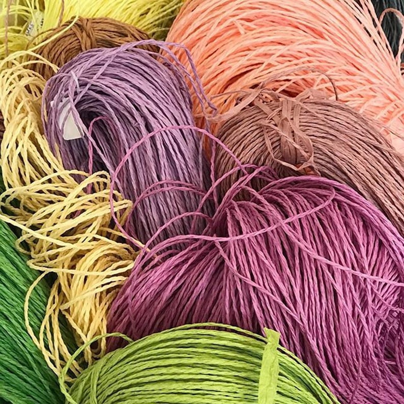 May include: A close-up of a variety of colorful paper cords, including yellow, orange, purple, pink, and green. The cords are twisted and piled together, creating a textured and colorful display.
