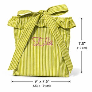 Pu&ograve; includere: Una borsa in tessuto a righe verde lime e bianche con bordo superiore arricciato e un fiocco. Il nome Ella &egrave; ricamato in corsivo rosa sul davanti. La borsa misura 23 cm di larghezza per 19 cm di altezza, come indicato dalle misure visibili.