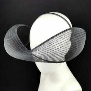 Può includere: Un cappello in rete nera con un'ampia tesa e una forma curva. Il cappello è realizzato in un materiale fine e delicato e ha un design moderno e astratto.