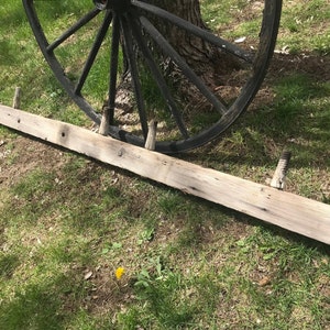 May include: A long, weathered wooden plank with metal spikes protruding from the top. The plank is lying on a grassy surface.