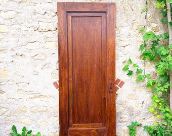 May include: A rectangular wooden door with a rich, dark brown stained finish. The door features a single large vertical recessed panel in the center, a wider bottom rail, and a small, dark metal escutcheon plate mounted on the right side.