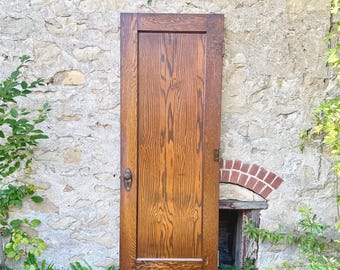 May include: A rectangular wooden door featuring a prominent vertical grain pattern in a medium brown finish. The door includes a single central panel, a dark metal round doorknob, and a matching metal keyhole plate mounted on the left side.