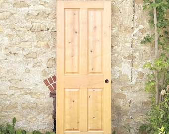 May include: A light-coloured wooden door featuring a four-panel design with visible natural wood grain and knots. The door has a smooth finish and a single circular hole on the right side intended for a door handle or knob installation.