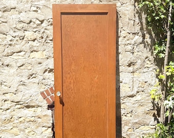 May include: A rectangular wooden door with a medium brown finish and a visible wood grain pattern. The door features a single large central panel and a clear, round glass doorknob attached to the left side of the frame.