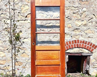 Puede incluir: Una puerta rectangular de madera con un acabado marrón cálido, que presenta una sección superior con tres paneles de vidrio horizontales y una sección inferior con dos paneles rectangulares empotrados. Se ve un orificio circular.