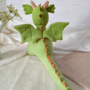 May include: A green plush dragon toy with orange spikes down its back and tail. The dragon has large wings and a small head with two horns.