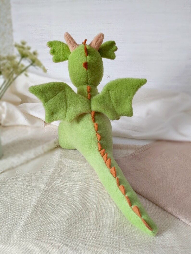 May include: A green plush dragon toy with orange spikes down its back and tail. The dragon has large wings and a small head with two horns.