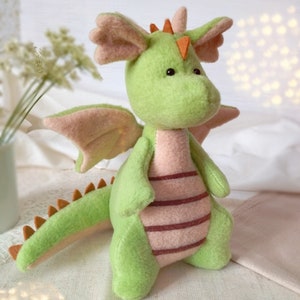 May include: A green plush dragon toy with pink wings and a striped belly. The dragon has orange horns and black eyes.