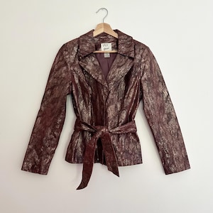 May include: A burgundy snakeskin-patterned jacket with a matching tie belt. The jacket features a collared neckline and long sleeves. The label reads "VRO sport".