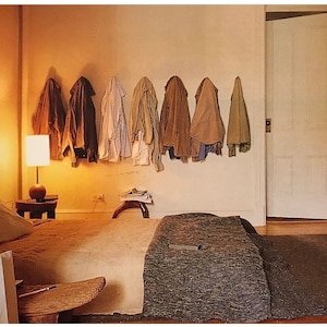 Pode incluir: Um quarto com uma cama, uma lâmpada e uma mesa de cabeceira de madeira. Há várias jaquetas penduradas na parede.