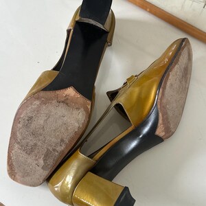 Puede incluir: Un par de zapatos vintage de charol dorado con punta cuadrada y tac&oacute;n ancho. Los zapatos tienen una correa en la parte superior del pie y una suela negra. Los tacones miden aproximadamente 7,6 cm de alto.