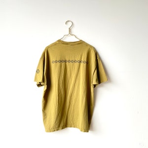 May include: A mustard yellow t-shirt with a black graphic print of a repeating pattern of circles with the number 90 inside each circle.