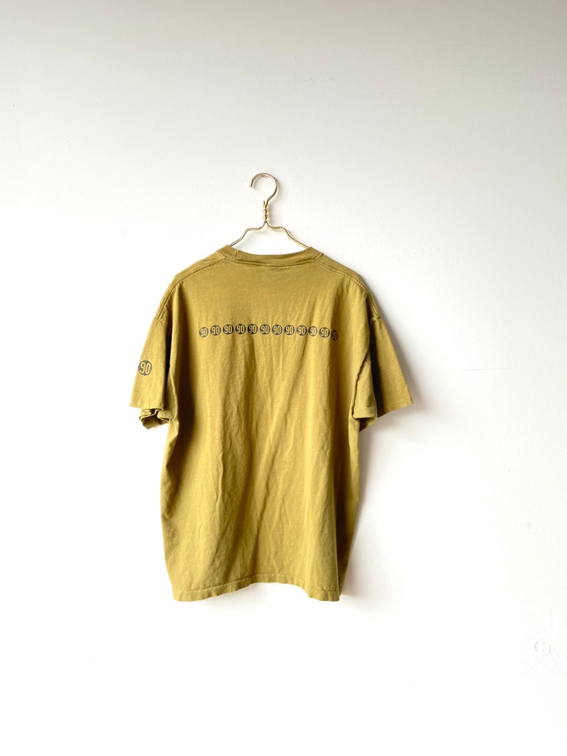 May include: A mustard yellow t-shirt with a black graphic print of a repeating pattern of circles with the number 90 inside each circle.