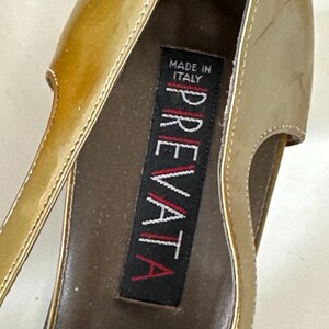 Puede incluir: Primer plano de un zapato de tac&oacute;n alto dorado. El zapato tiene un acabado brillante y un dise&ntilde;o recortado. El interior presenta una etiqueta que dice "MADE IN ITALY" y el nombre de la marca "PREVATA".