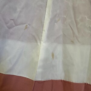 May include: Close-up of a garment with a color block design. The top portion is a light cream color, the middle is a pale yellow, and the bottom is a muted rose color. There are several small stains on the cream and yellow sections.