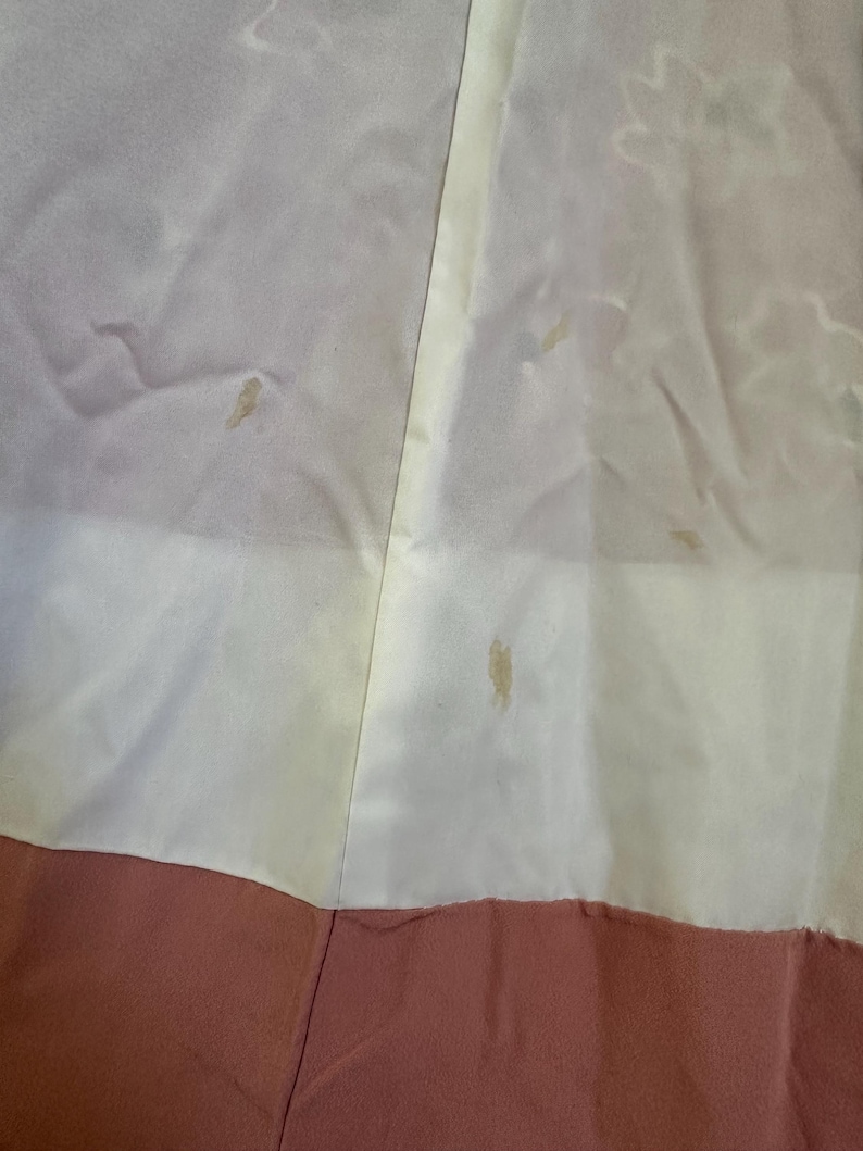 May include: Close-up of a garment with a color block design. The top portion is a light cream color, the middle is a pale yellow, and the bottom is a muted rose color. There are several small stains on the cream and yellow sections.