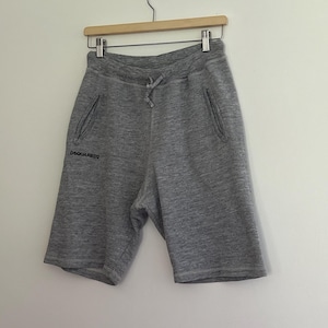 May include: Gray sweat shorts with a drawstring waist and side pockets, hanging on a wooden hanger. The shorts have the text "DSQUARED2" printed on the left leg.