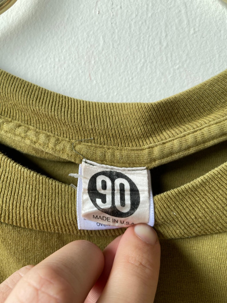 May include: A green t-shirt with a white tag that says "90" in a circle and "Made in U.S.A."