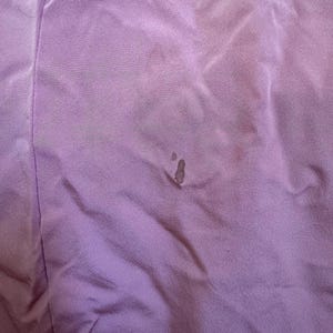 May include: Close-up of a lavender fabric with visible wrinkles and dark spots. The fabric appears to be a soft material, possibly a garment or textile. The image highlights the texture and color variations.