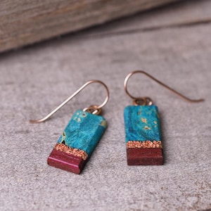 May include: A pair of dangle earrings with a copper wire hook and a rectangular turquoise and maroon resin pendant.