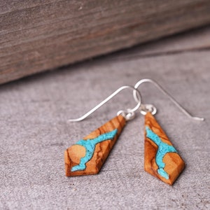 May include: A pair of wooden earrings with silver hooks. The earrings are shaped like teardrops and have a blue and brown marbled pattern.