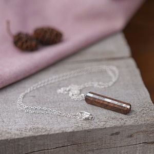 May include: A silver chain necklace with a wooden pendant featuring a thin strip of iridescent mother of pearl inlay.