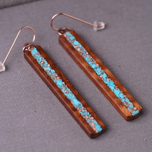 May include: A pair of long, rectangular earrings with a wooden base and a turquoise inlay. The earrings have a copper wire hook.