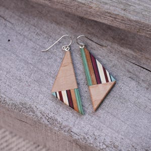 May include: A pair of geometric wooden earrings. Each earring is a triangle with a light wood base and a section of colorful stripes in shades of green, burgundy, and cream. The earrings have silver-colored ear wires.