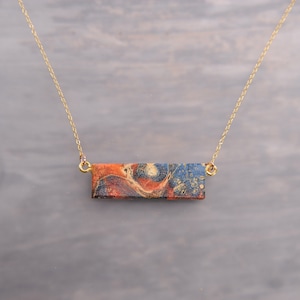 May include: A gold chain necklace with a rectangular pendant featuring a marbled design in shades of blue, red, and gold.