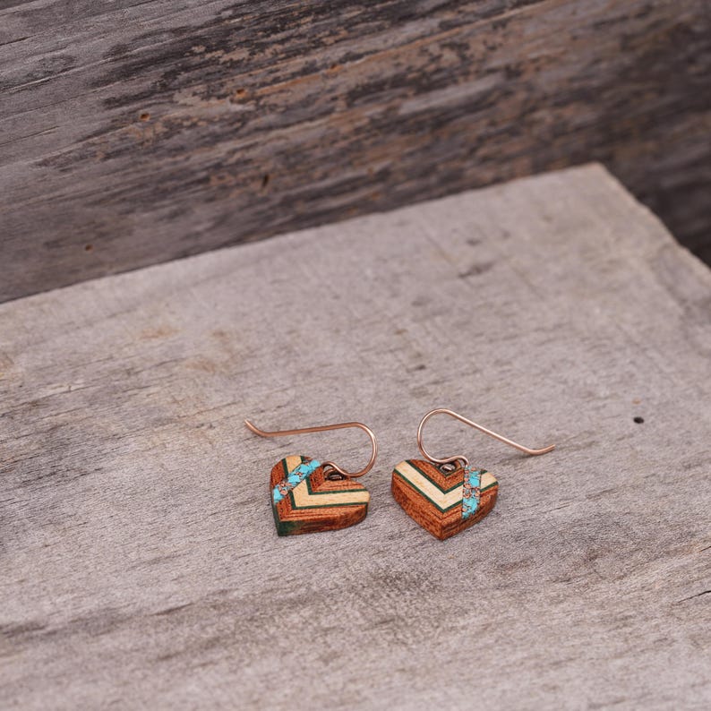 May include: A pair of heart-shaped earrings made of wood with a geometric pattern and turquoise accents. The earrings have a copper wire hook.