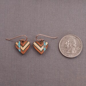 May include: A pair of heart-shaped earrings made of wood with a chevron pattern and turquoise accents. The earrings are about the size of a quarter.