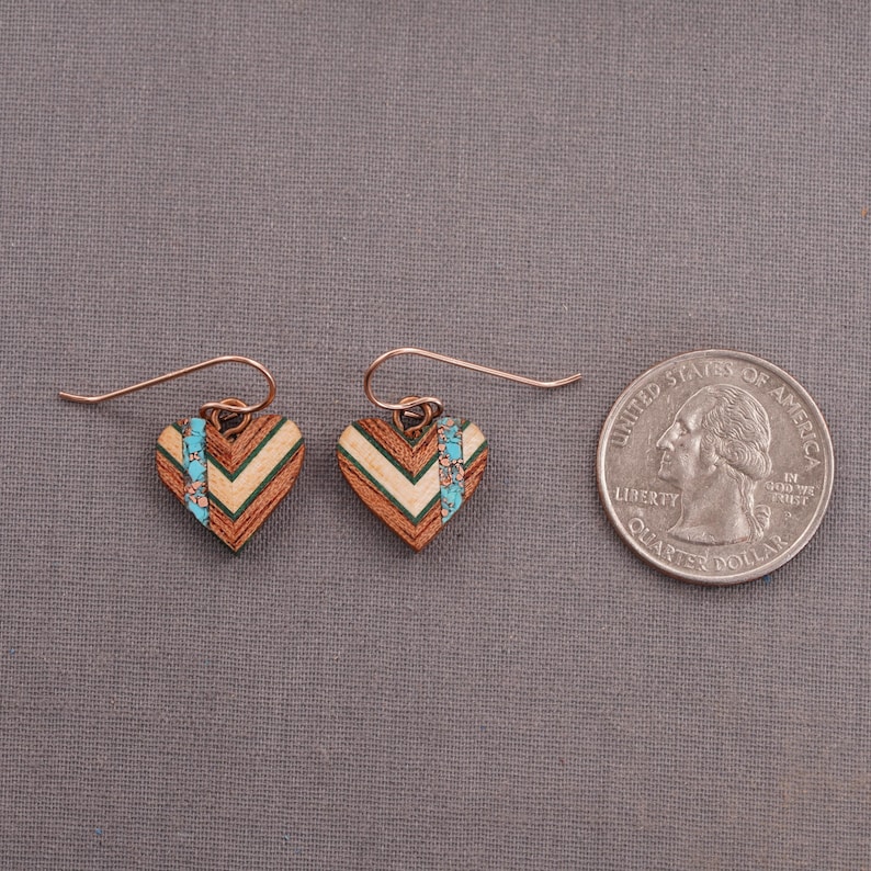 May include: A pair of heart-shaped earrings made of wood with a chevron pattern and turquoise accents. The earrings are about the size of a quarter.