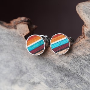May include: A pair of round wood earrings with a multi-colored striped pattern in shades of orange, red, blue, and white. The earrings have silver posts.