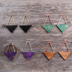 May include: Six pairs of triangle-shaped earrings with different coloured wood and metal accents. The earrings are made with gold, silver, copper, and black metal wire. The wood is in shades of black, green, purple, and brown.