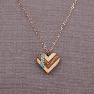 May include: A rose gold chain necklace with a heart-shaped pendant made of wood with turquoise and brown inlay.
