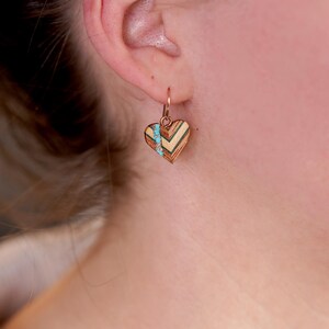 May include: A pair of heart-shaped earrings with a geometric wood pattern and turquoise accents. The earrings are made of wood and have a gold-tone finish.