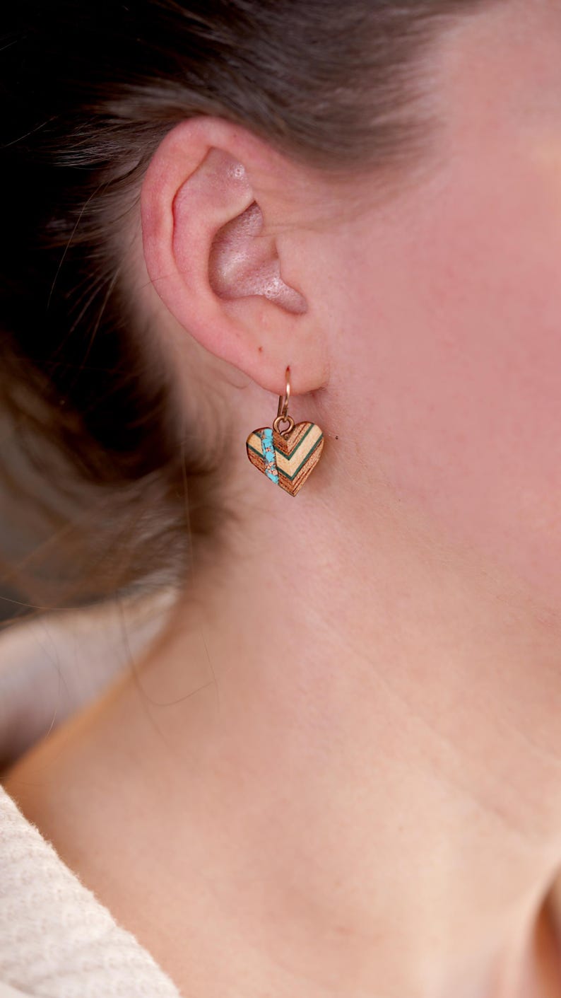 May include: A pair of heart-shaped earrings with a geometric wood pattern and turquoise accents. The earrings are made of wood and have a gold-tone finish.