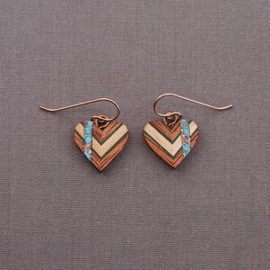 May include: A pair of wooden heart-shaped earrings with a chevron pattern and turquoise accents. The earrings are made of wood and have a copper wire hook.