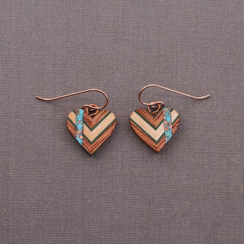 May include: A pair of wooden heart-shaped earrings with a chevron pattern and turquoise accents. The earrings are made of wood and have a copper wire hook.